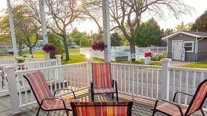 A wooden deck with a table and striped chairs, surrounded by a white fence and trees. - Capt.'s Inn & Suites (Alexandria Bay)