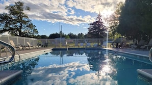A clear swimming pool with a metal railing, surrounded by lounge chairs and a fenced area. - Capt.'s Inn & Suites (Alexandria Bay)