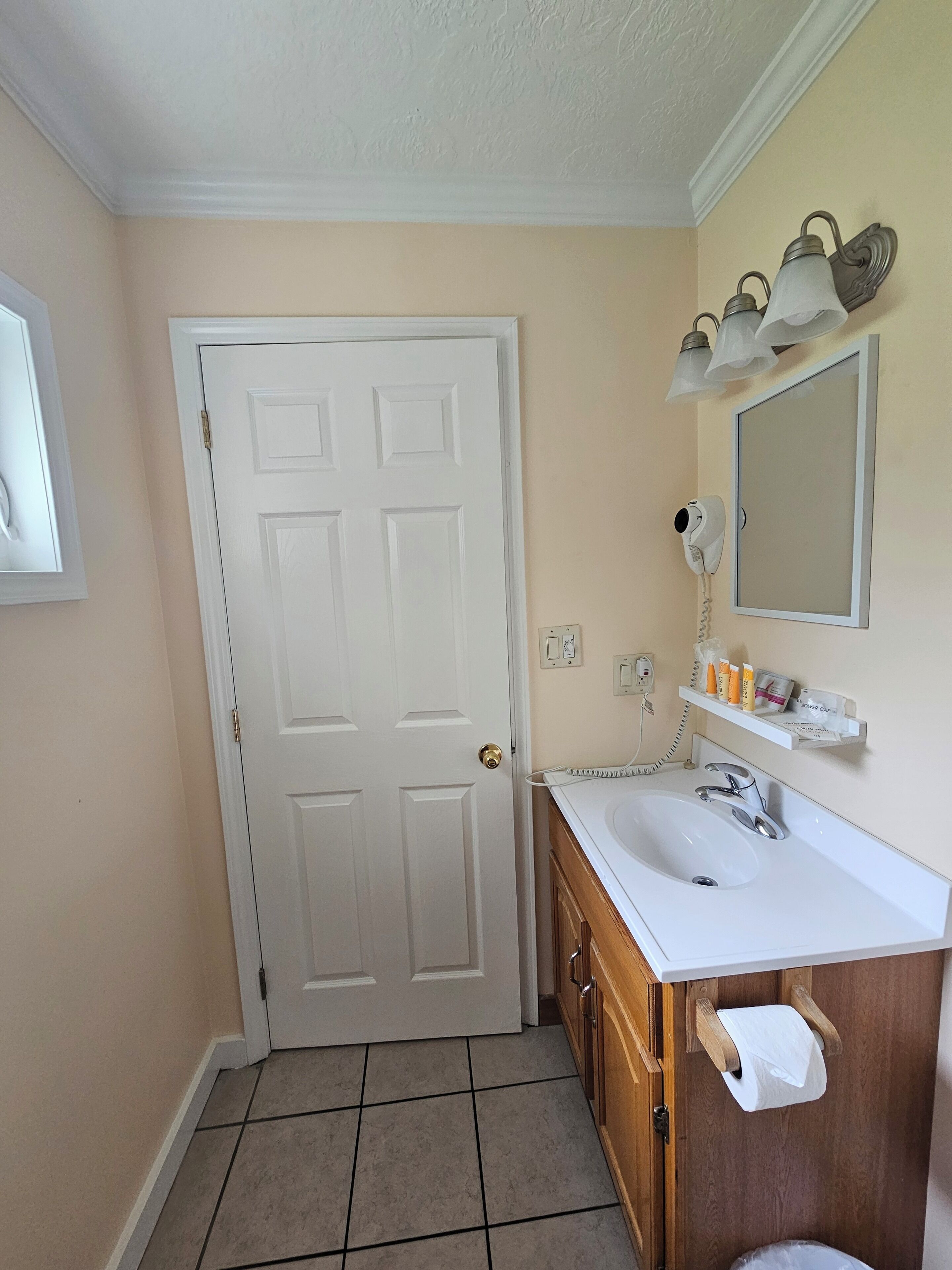 A bathroom with a white door, a vanity with a sink, a mirror, and a towel rack.