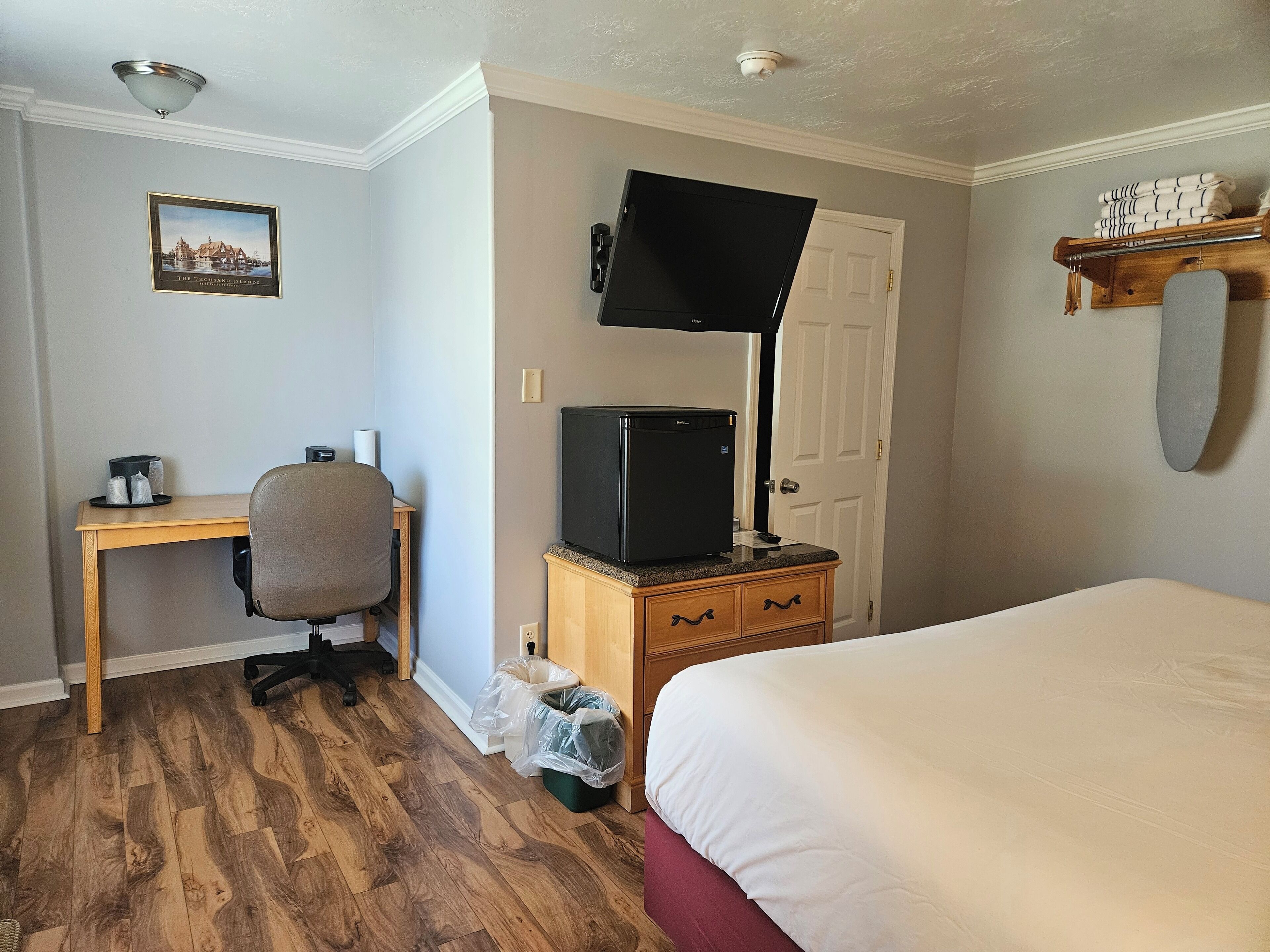Une chambre d’hôtel avec un bureau en bois, une télévision, un lit et une petite étagère avec des serviettes.