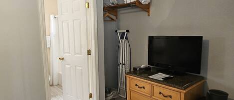 Una habitación con un aparador de madera, un televisor de pantalla plana, un estante con toallas dobladas y una puerta que da a otra habitación.