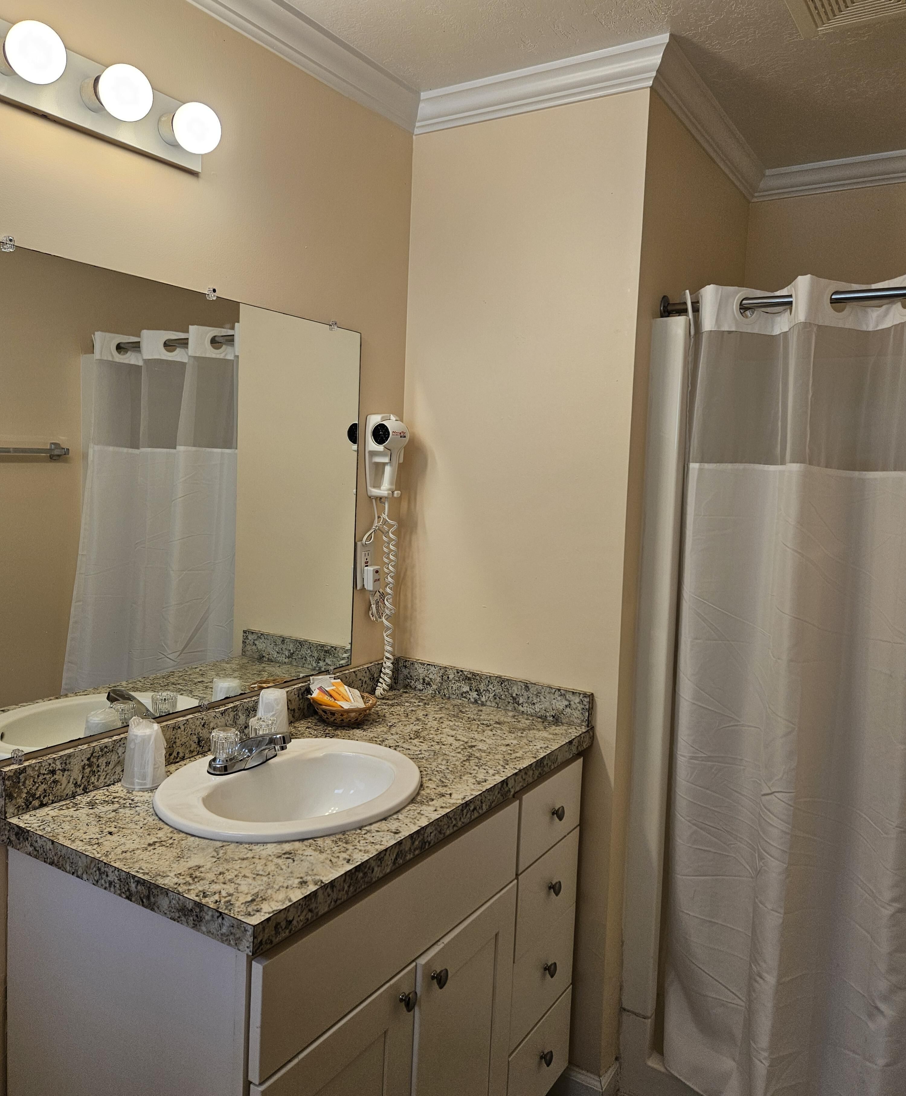 A bathroom with a sink, mirror, vanity, and a shower curtain.