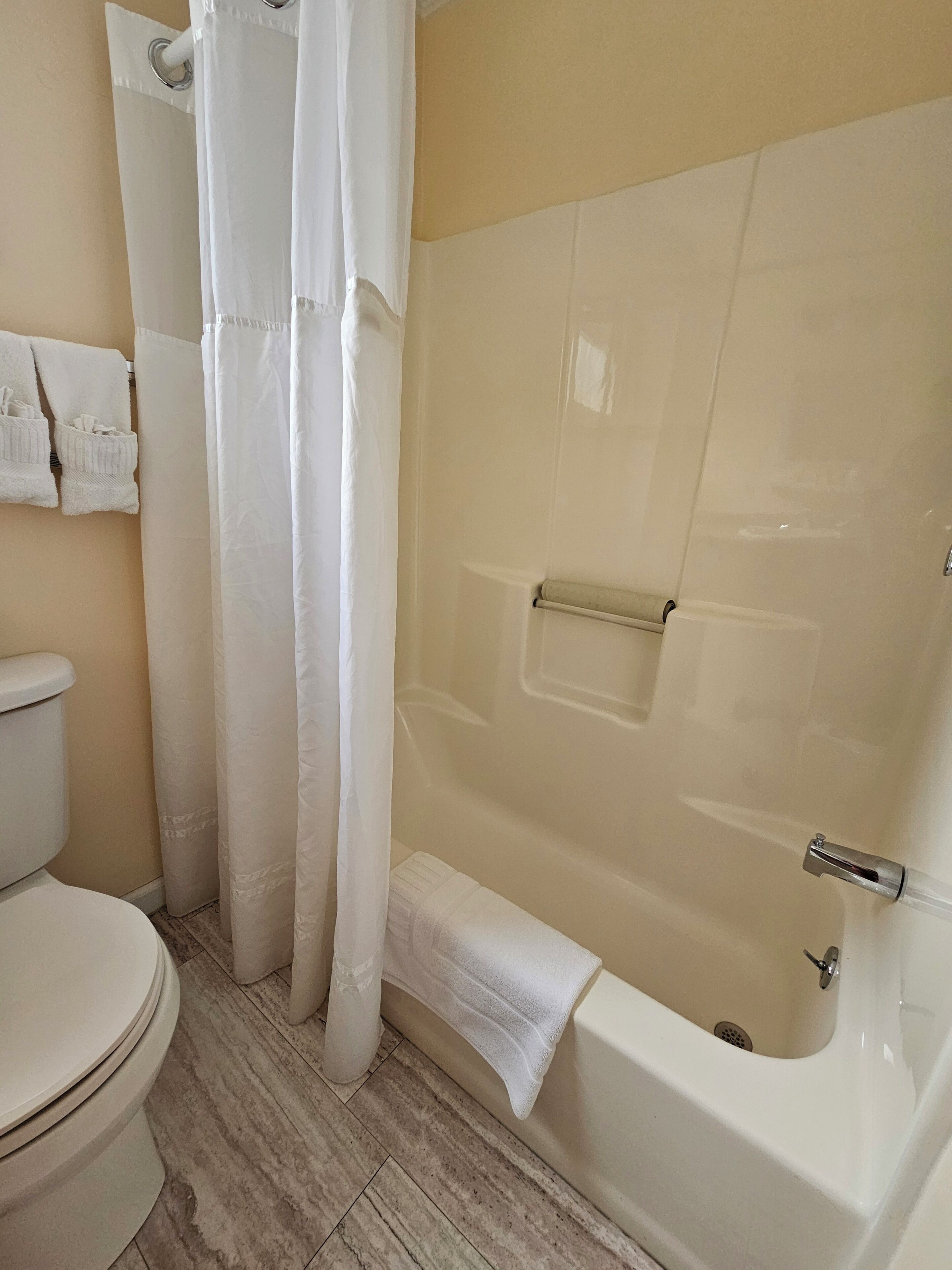 A bathroom with a toilet, a bathtub with a shower curtain, and a towel rack with towels.