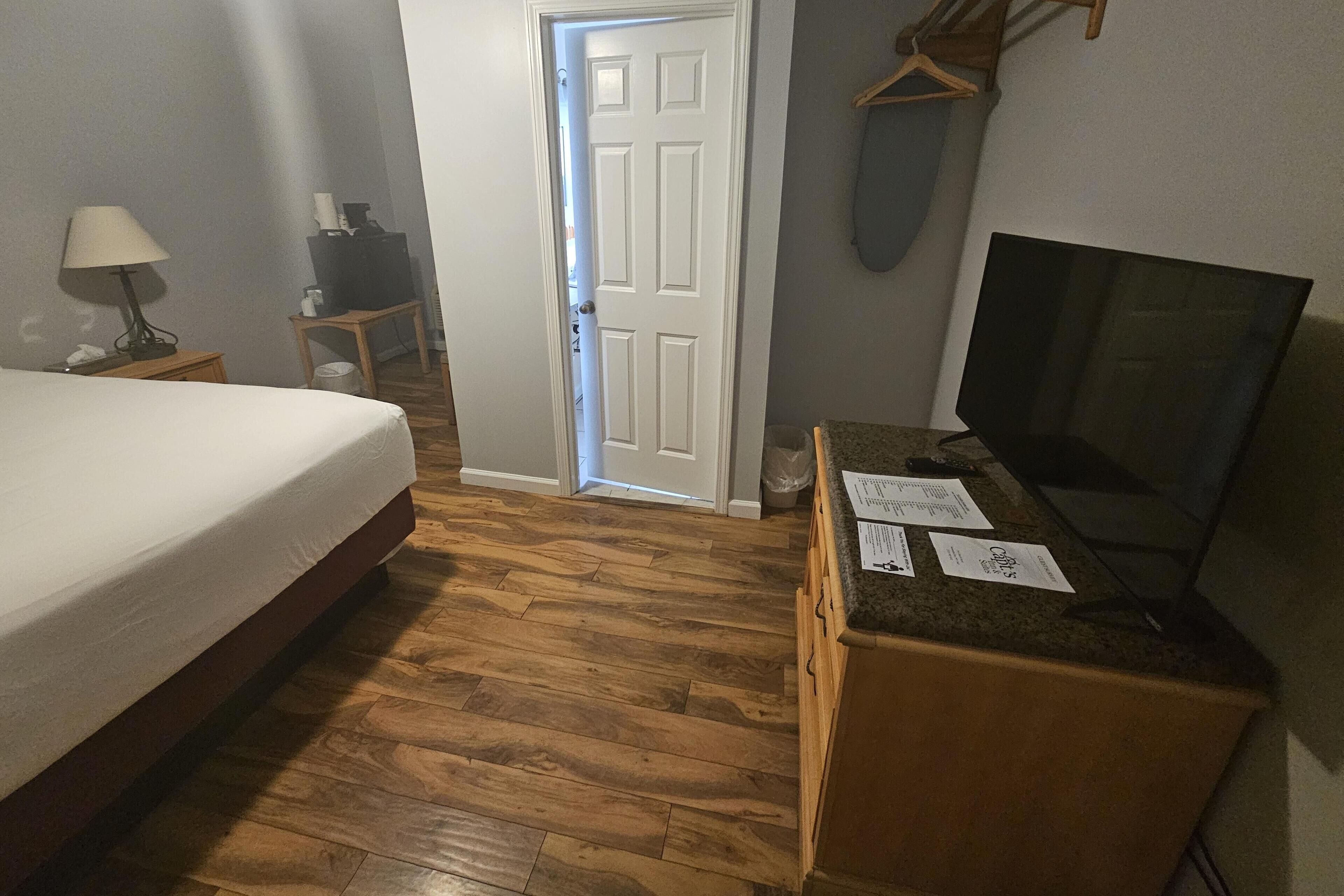 Una habitación de hotel con una cama, un escritorio con papeles, un televisor y una puerta que da a otra habitación.