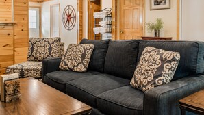 A cozy living room with a dark grey sofa, patterned cushions, a wooden coffee table, and a star compass wall decoration. - Capt.'s Inn & Suites (Alexandria Bay)