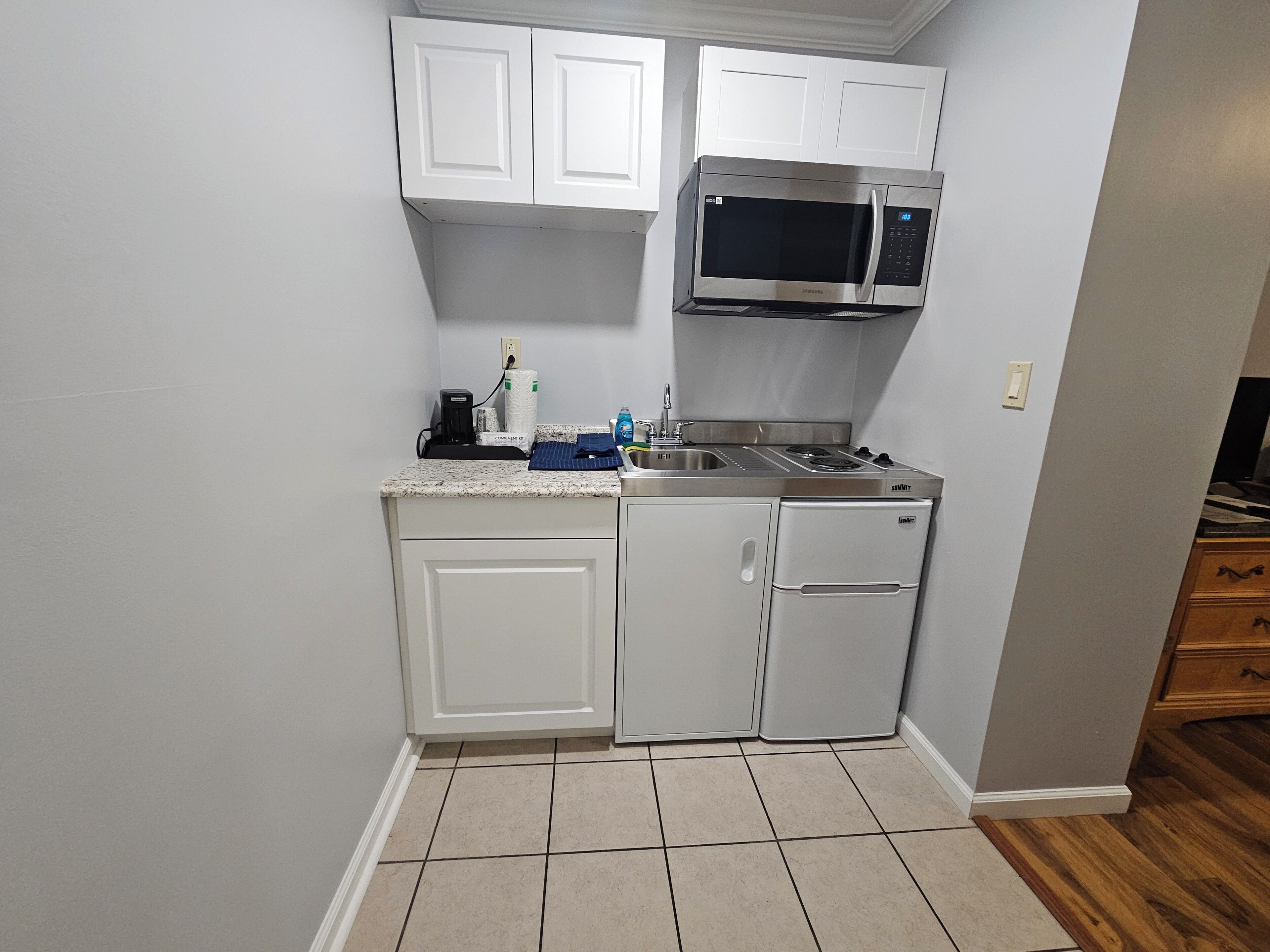 A compact kitchen with white cabinets, a built-in microwave, a sink, and a small refrigerator.