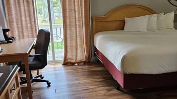 Habitación de hotel con escritorio de madera, una silla, una cama con ropa blanca y un ventanal con cortinas.