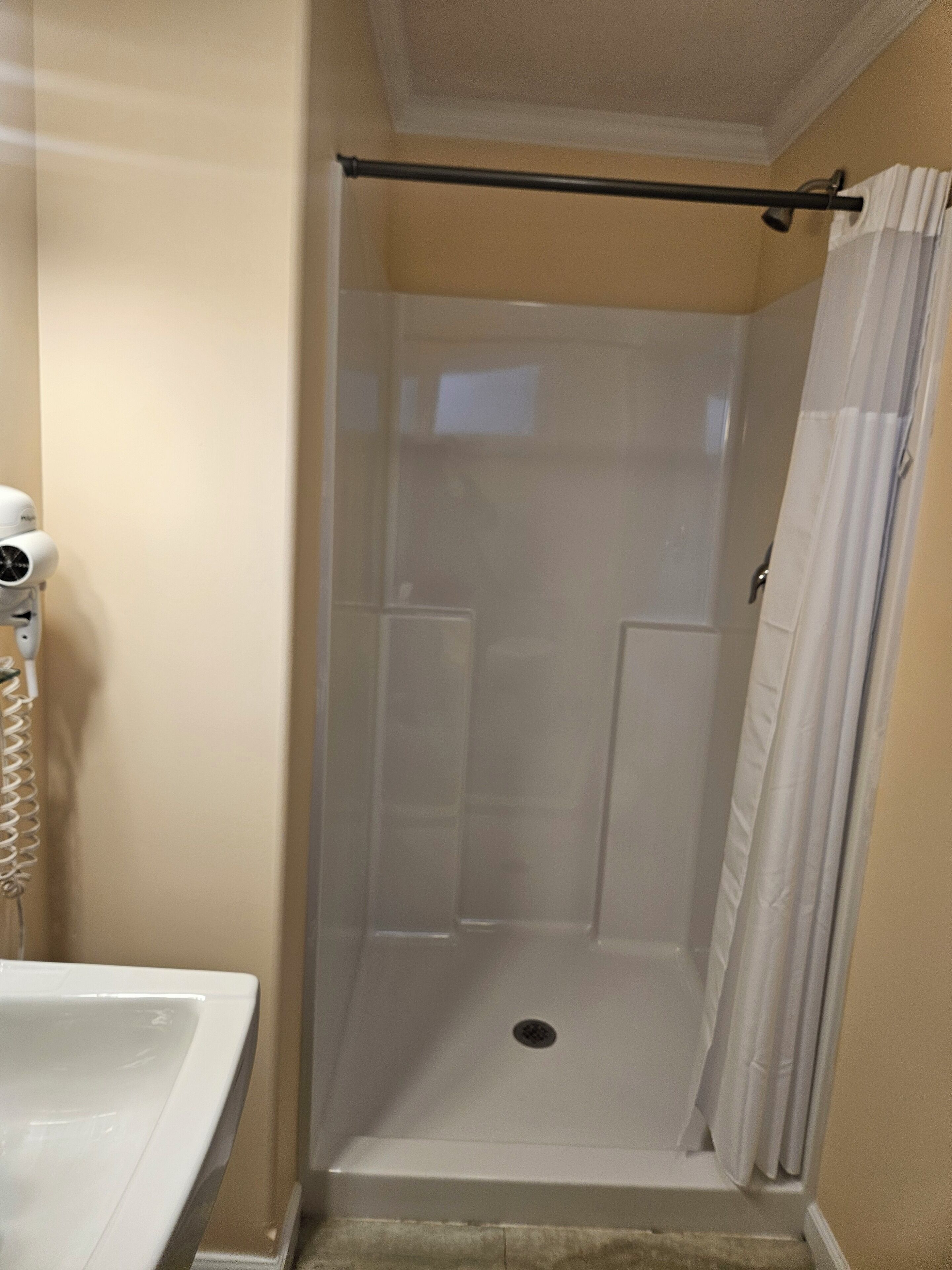 A shower area with a glass door, a towel rack, and a white shower curtain.