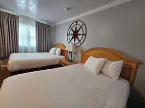A hotel room with two beds, a wooden headboard, a wall clock, and a window with curtains.