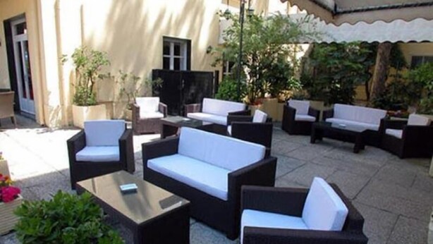 An outdoor patio area with multiple seating arrangements, including sofas and chairs, surrounded by potted plants and a tiled floor.