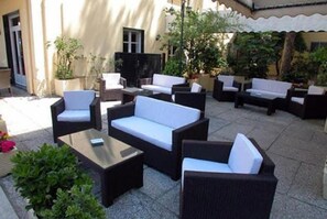 An outdoor patio area with multiple seating arrangements, including sofas and chairs, surrounded by potted plants and a tiled floor. - Hotel San Martino (Riccione)