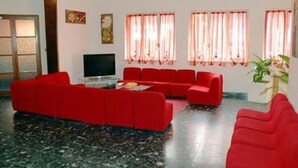 A living room with red sofas, a flat-screen TV, and windows with pink curtains.