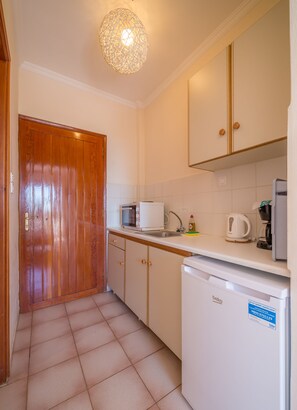 Una cocina compacta con puerta de madera, armarios blancos, horno empotrado, cafetera y lavavajillas.