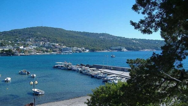 A coastal marina with boats docked, a pier, and a hillside town in the background. - 123 Soleil Studios (Aegina)