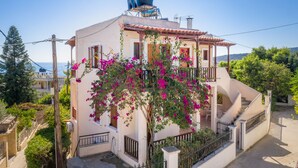 A two-story house with a water tank on the roof, surrounded by greenery and a clear sky. - 123 Soleil Studios (Aegina)