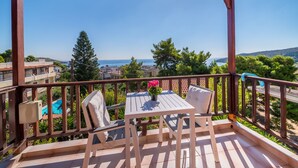 A wooden deck with a table and chairs, overlooking a swimming pool and a scenic view of the sea and hills. - 123 Soleil Studios (Aegina)