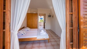 A bedroom with a wooden bed, white curtains, and a view of the outside. - 123 Soleil Studios (Aegina)