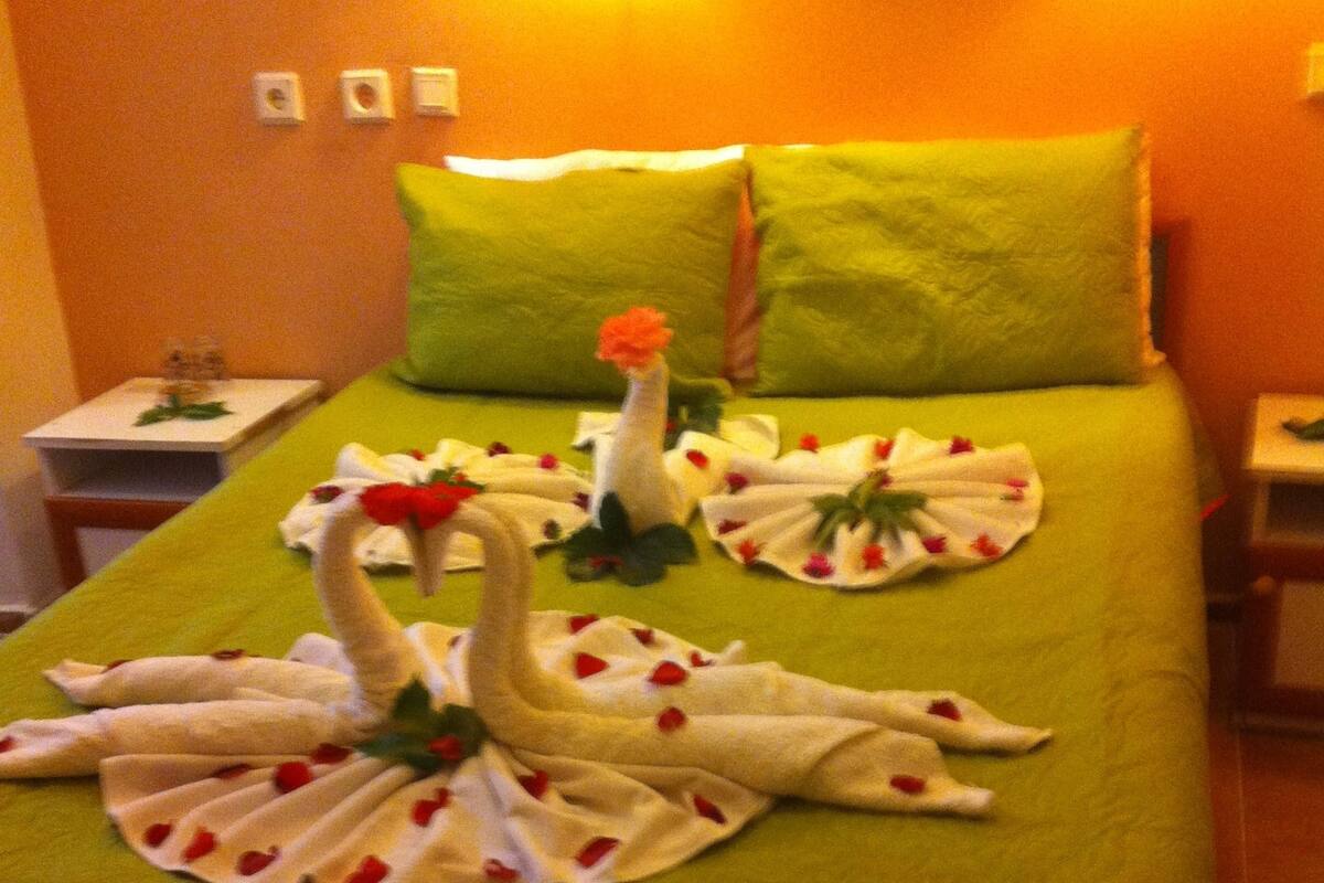 A hotel room with a bed covered in green sheets, two pillows, and a swan-shaped towel arrangement.