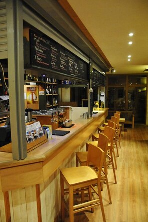 A bar area with a wooden counter, bar stools, and a menu board. - La Bérangère (Chamrousse)
