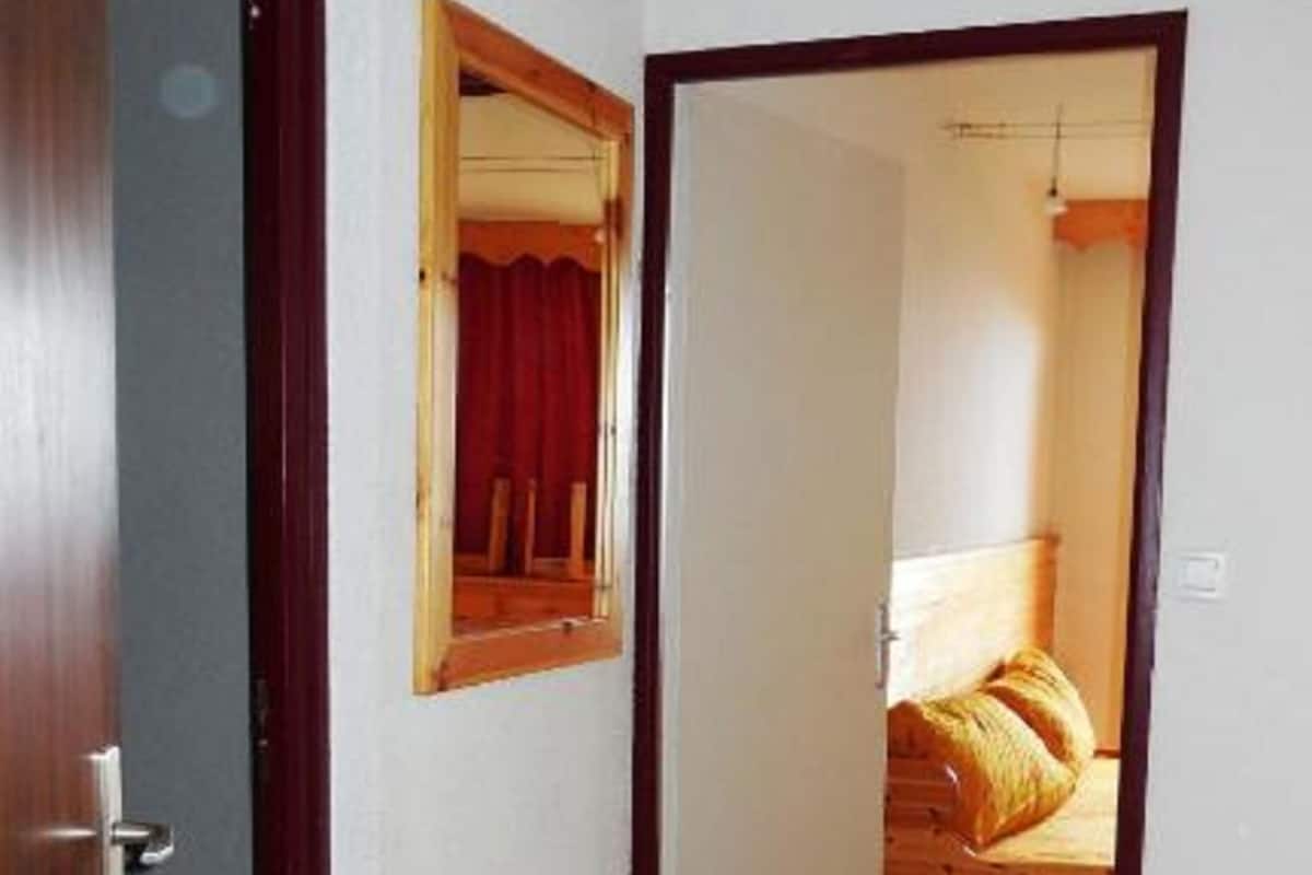 A narrow hallway with wooden flooring leading to a bedroom with a bed and a mirror on the wall.