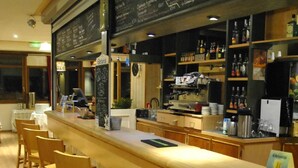A bar area with wooden chairs and a counter. There is a chalkboard menu above the counter listing various drinks. - La Bérangère (Chamrousse)