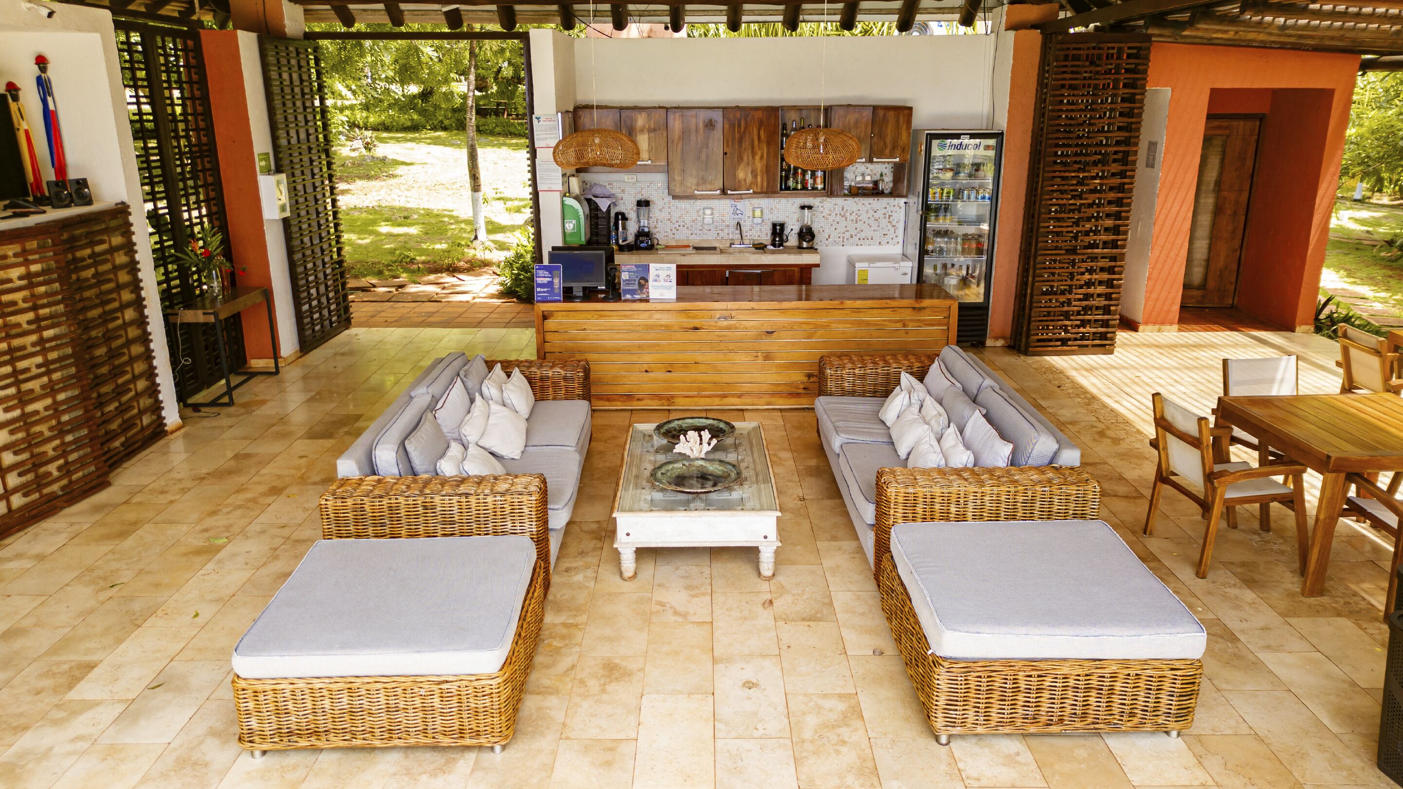 A covered outdoor seating area with wicker furniture, a coffee station, and a view of the garden.