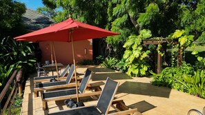 A sunlit outdoor seating area with lounge chairs and a red umbrella, surrounded by lush greenery and a wooden pergola. - Hotel Acantilado de La Tierra by On vacation (San Andrés)