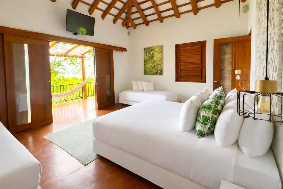 A bedroom with a large bed, a smaller bed, a TV, and a balcony with a view.