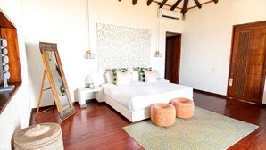 Un dormitorio con cama, mesitas de noche, un muro decorativo, una puerta de madera y una alfombra estampada.