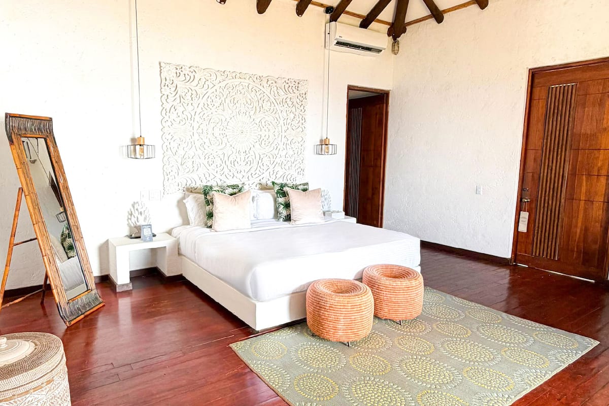 A bedroom with a bed, bedside tables, a decorative wall, a wooden door, and a patterned rug.
