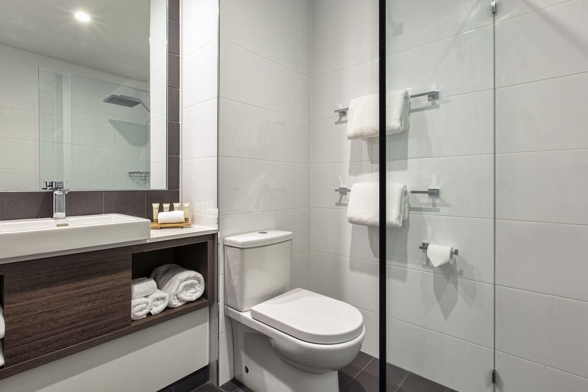 A modern bathroom with a glass shower enclosure, a white toilet, and a vanity with a mirror and toiletries.