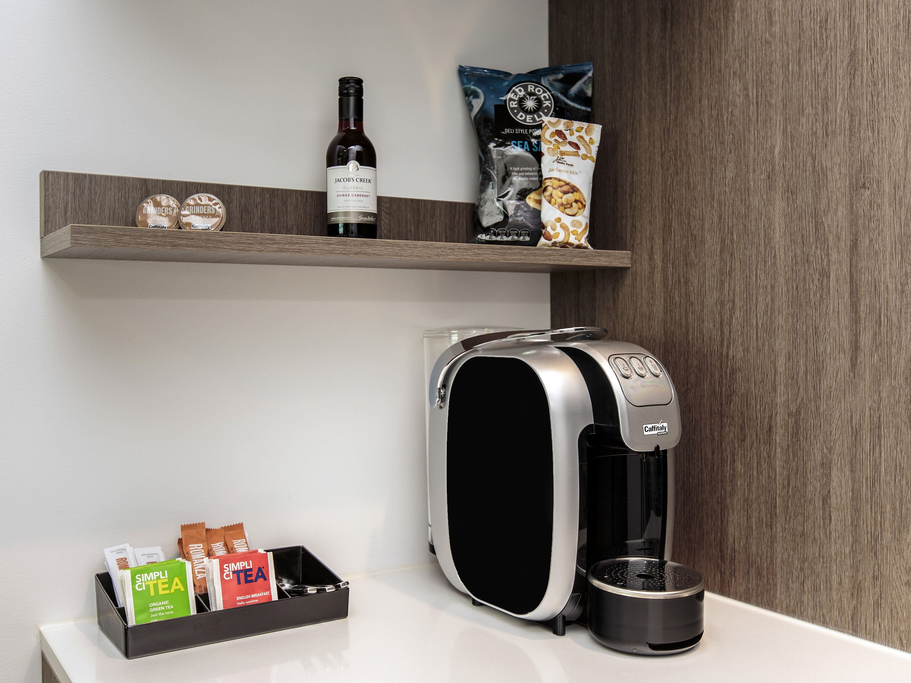 A modern kitchen with a coffee machine, a wine bottle, and tea packets on a shelf.
