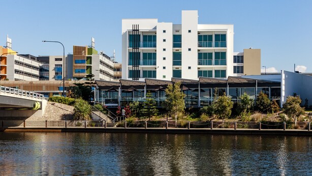 A modern building with a glass facade, a bridge, and a waterfront. - Mercure Sunshine Coast Kawana Waters (Birtinya)