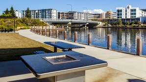 Un patio exterior con una parrilla y zona de estar con vista a un río, con edificios al fondo.