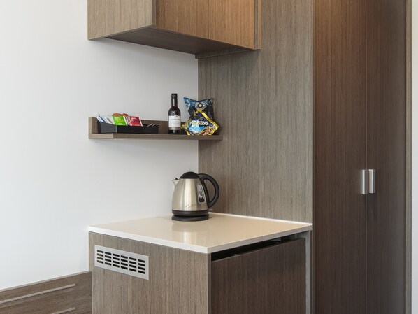 Una kitchenette con cafetera, bolsitas de té y una botella de vino sobre una repisa.