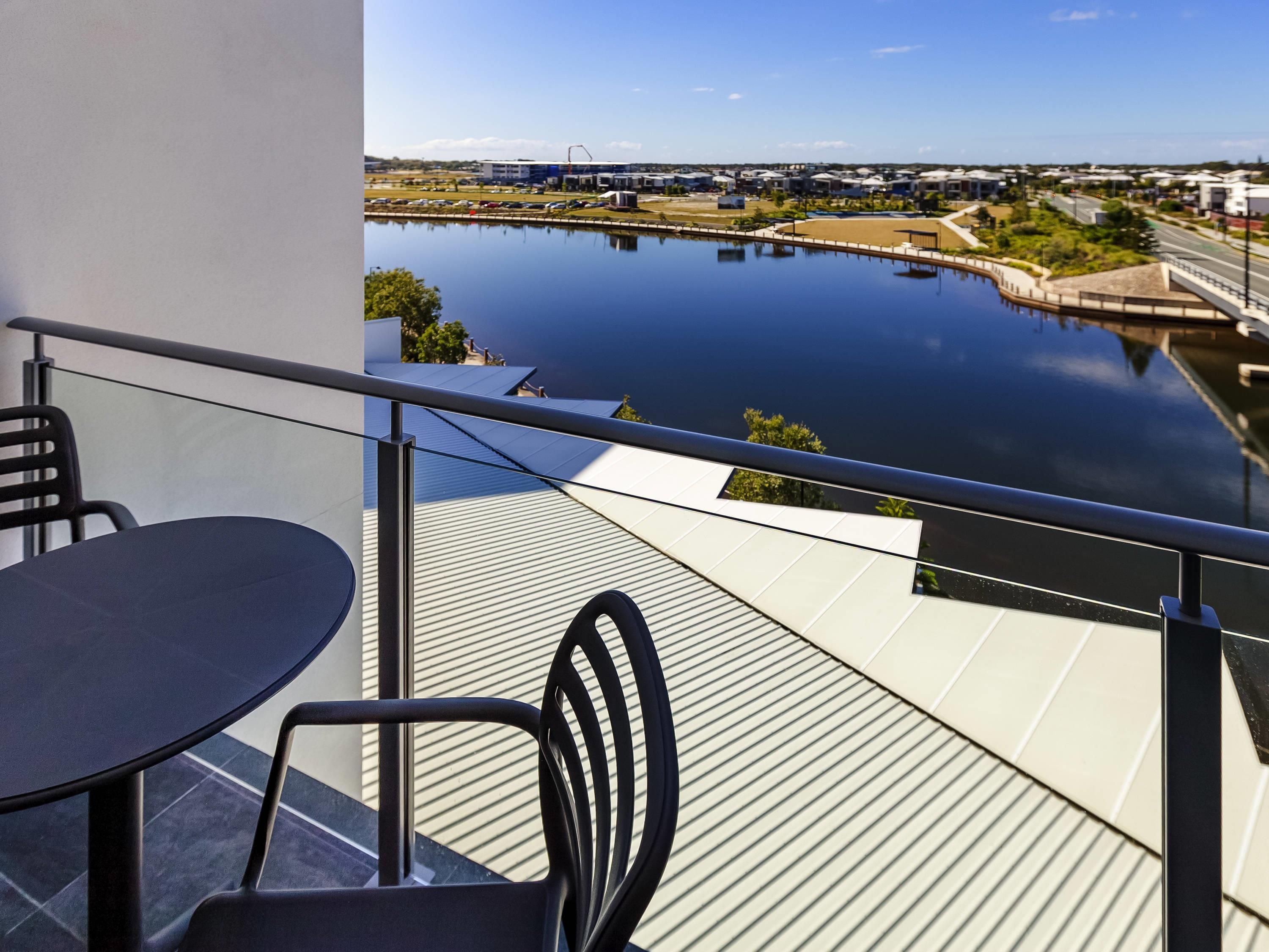 A balcony with a table and chairs overlooking a calm body of water and a distant cityscape.