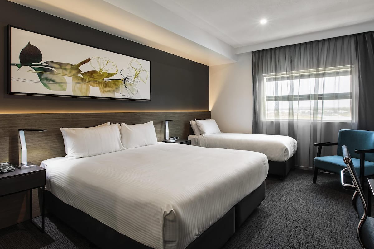 A hotel room with a large bed, a smaller bed, a desk with a lamp, a chair, and a window with curtains.