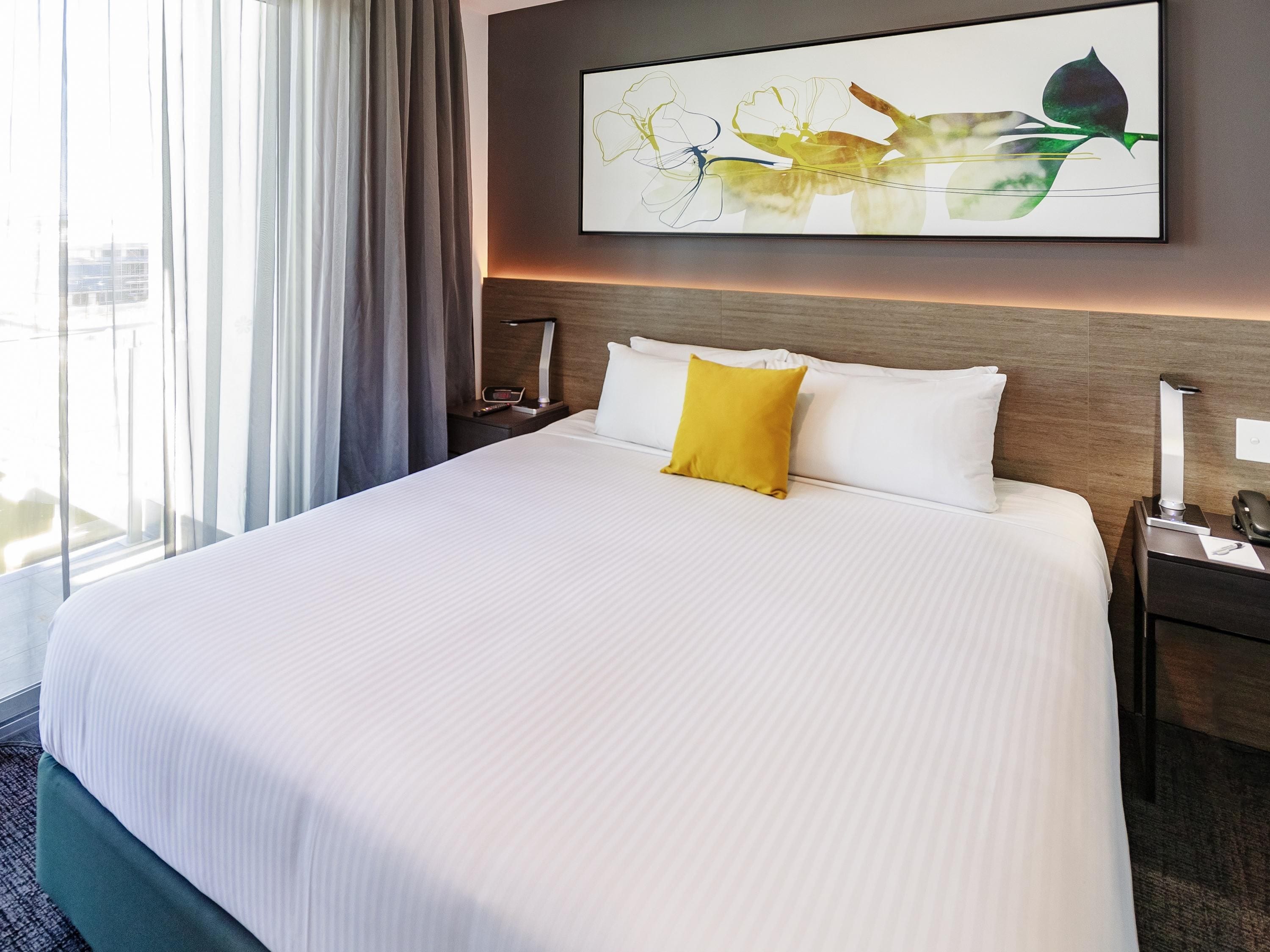 A hotel room with a large bed, a nightstand, a bedside table, a lamp, and a window with curtains.