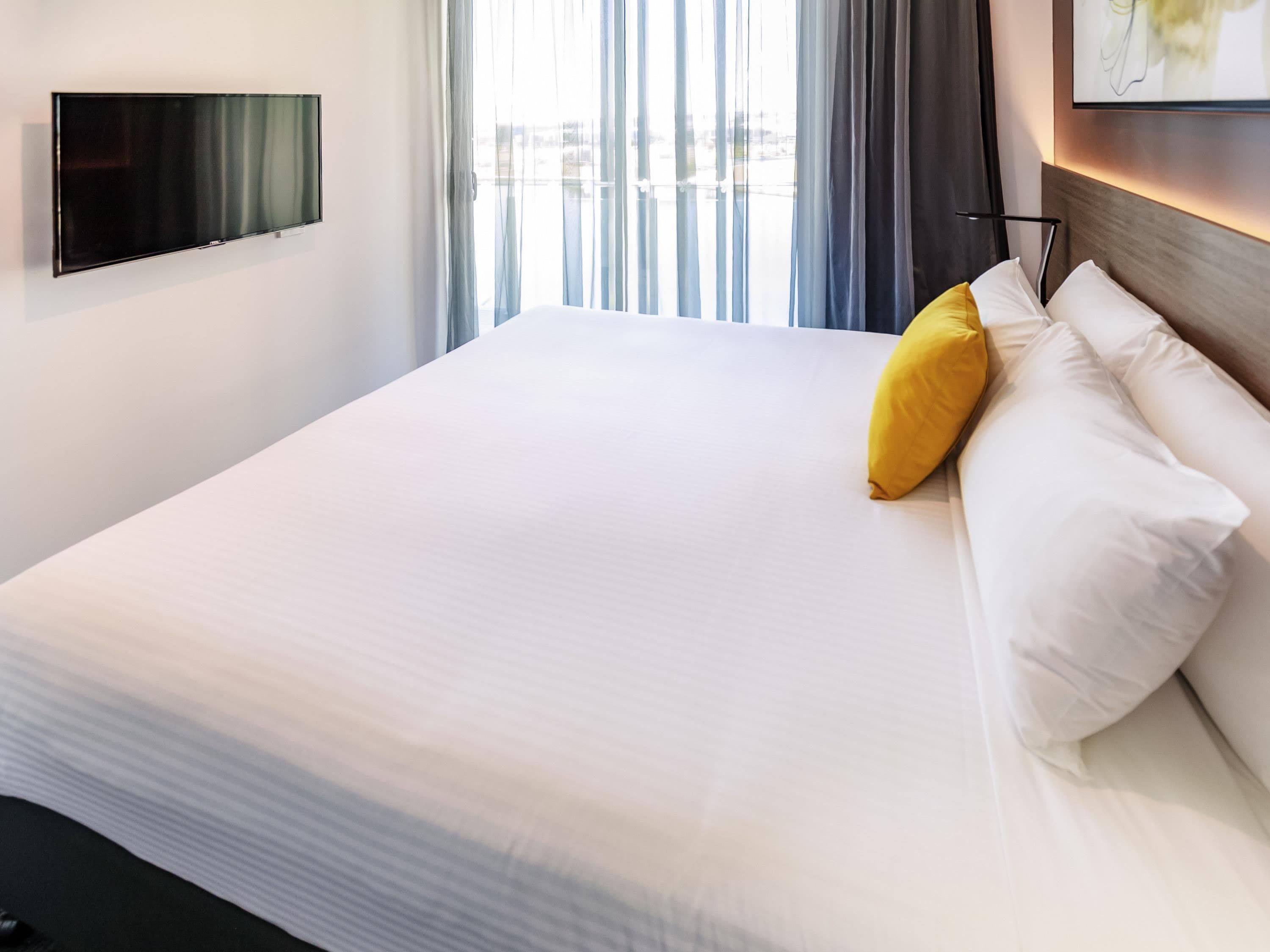 Une chambre d’hôtel avec un grand lit, un téléviseur à écran plat fixé au mur et une vue sur la ville par la fenêtre.