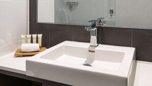 Ein modernes Badezimmer mit einem großen Spiegel, einem weißen Waschbecken und einer Dusche.