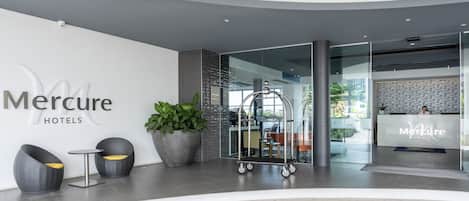Un moderno vestíbulo de hotel con mostrador de recepción, zona de estar y plantas en macetas.