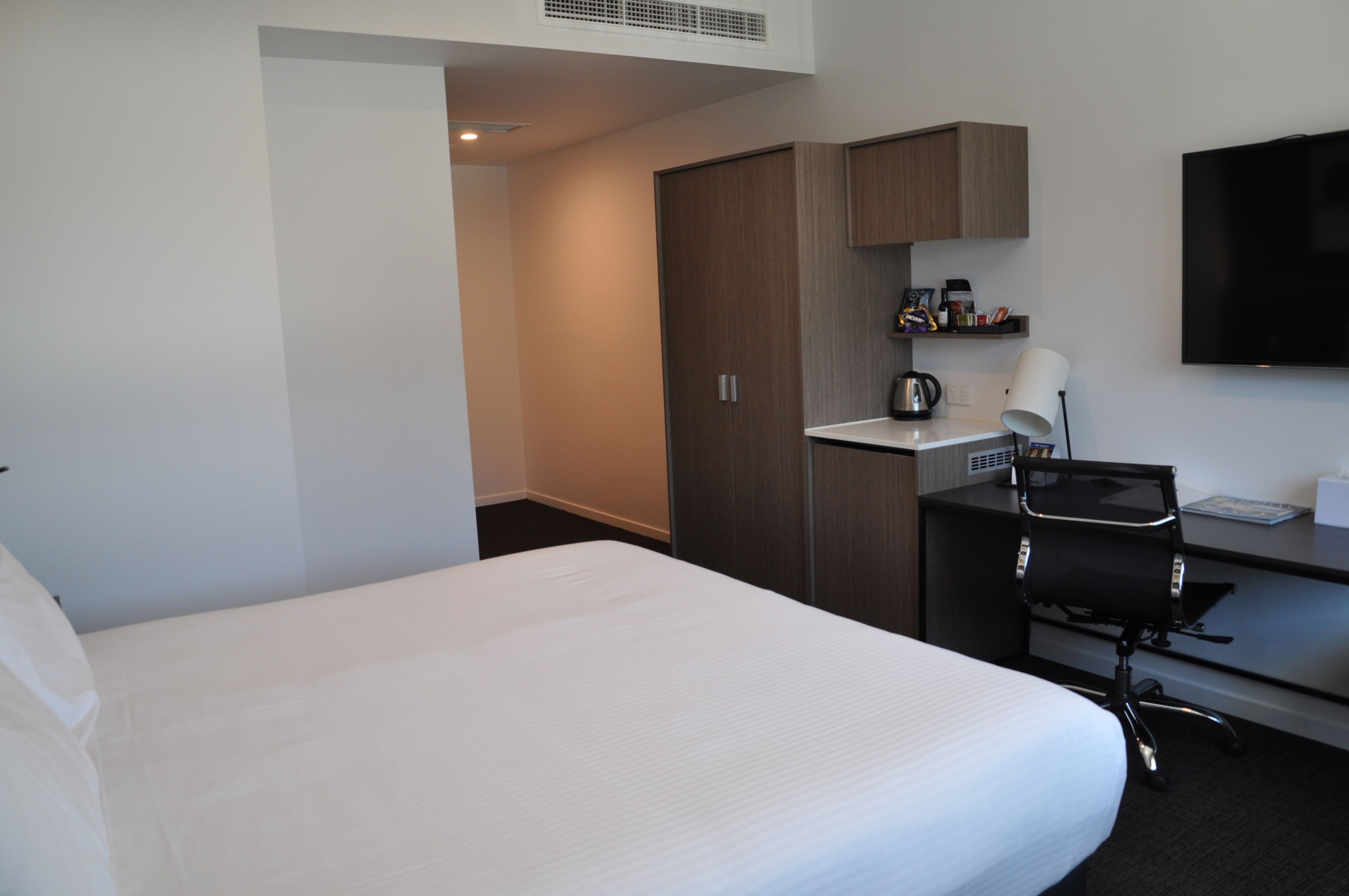 Hotelkamer met een groot bed, een bureau met stoel, een flatscreen televisie en een kitchenette.
