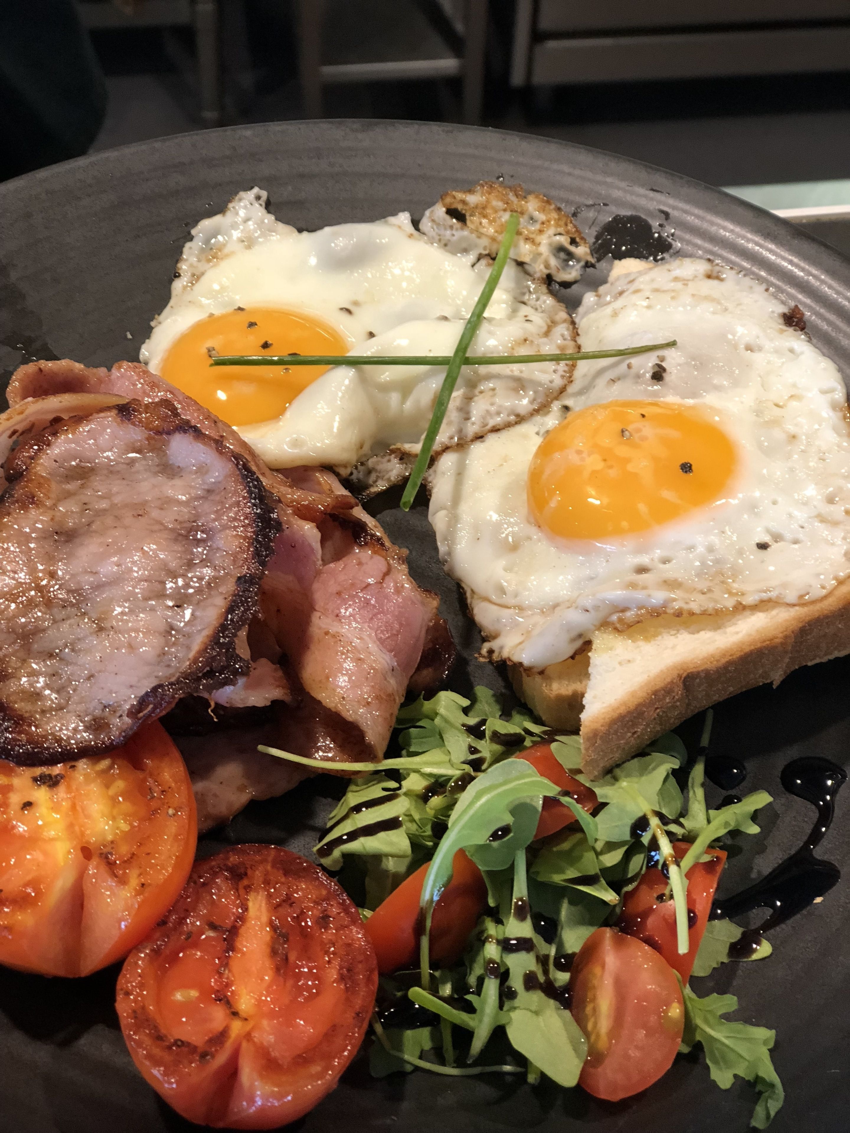 Une assiette de petit-déjeuner avec des œufs, du bacon, des tomates et des légumes verts.
