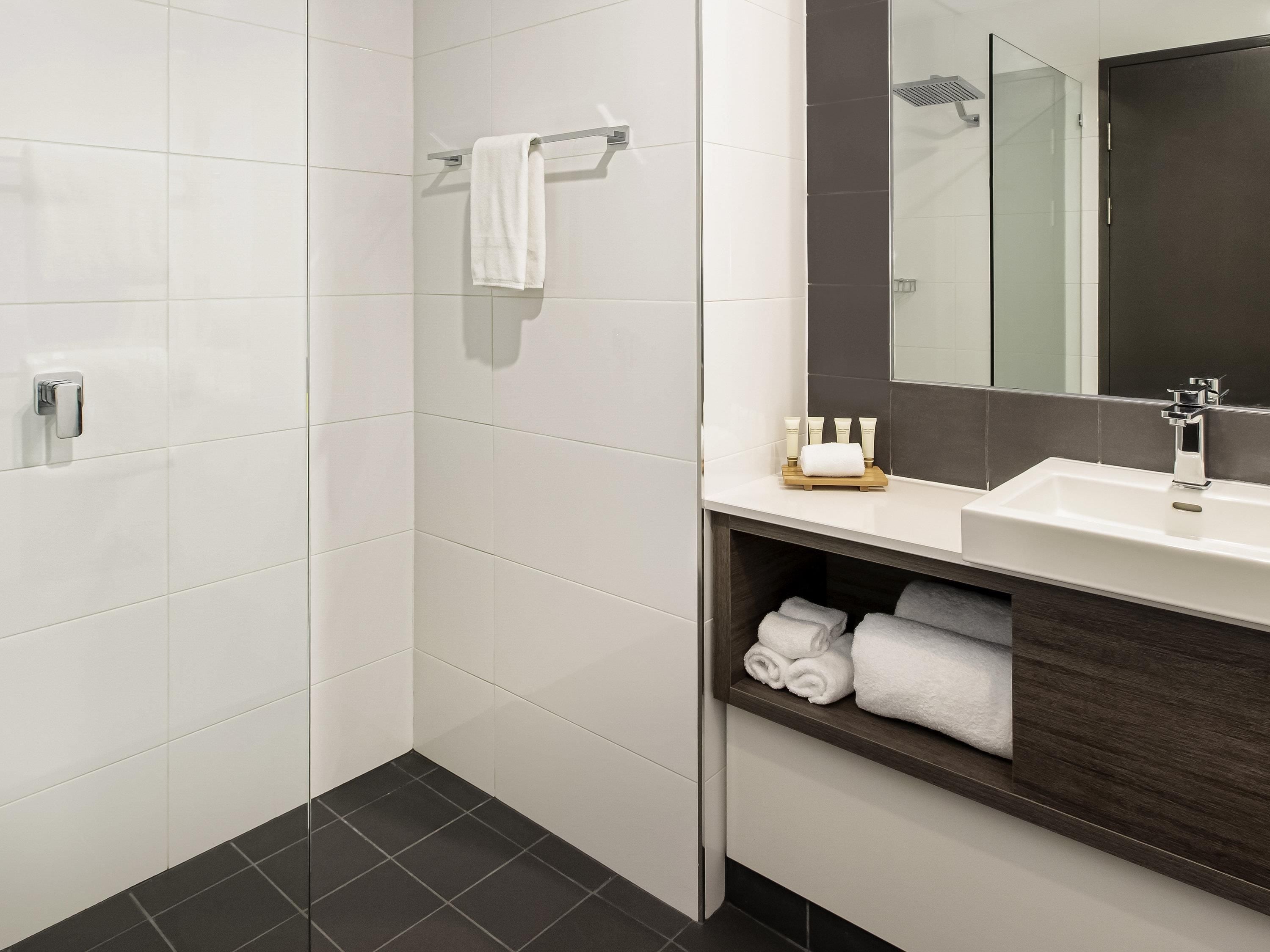 Une salle de bain moderne avec des carreaux blancs, un meuble-lavabo en bois foncé, un miroir et un espace douche.