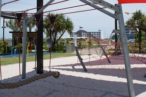 Un parque infantil con columpios, estructuras de escalada y un puente colgante.
