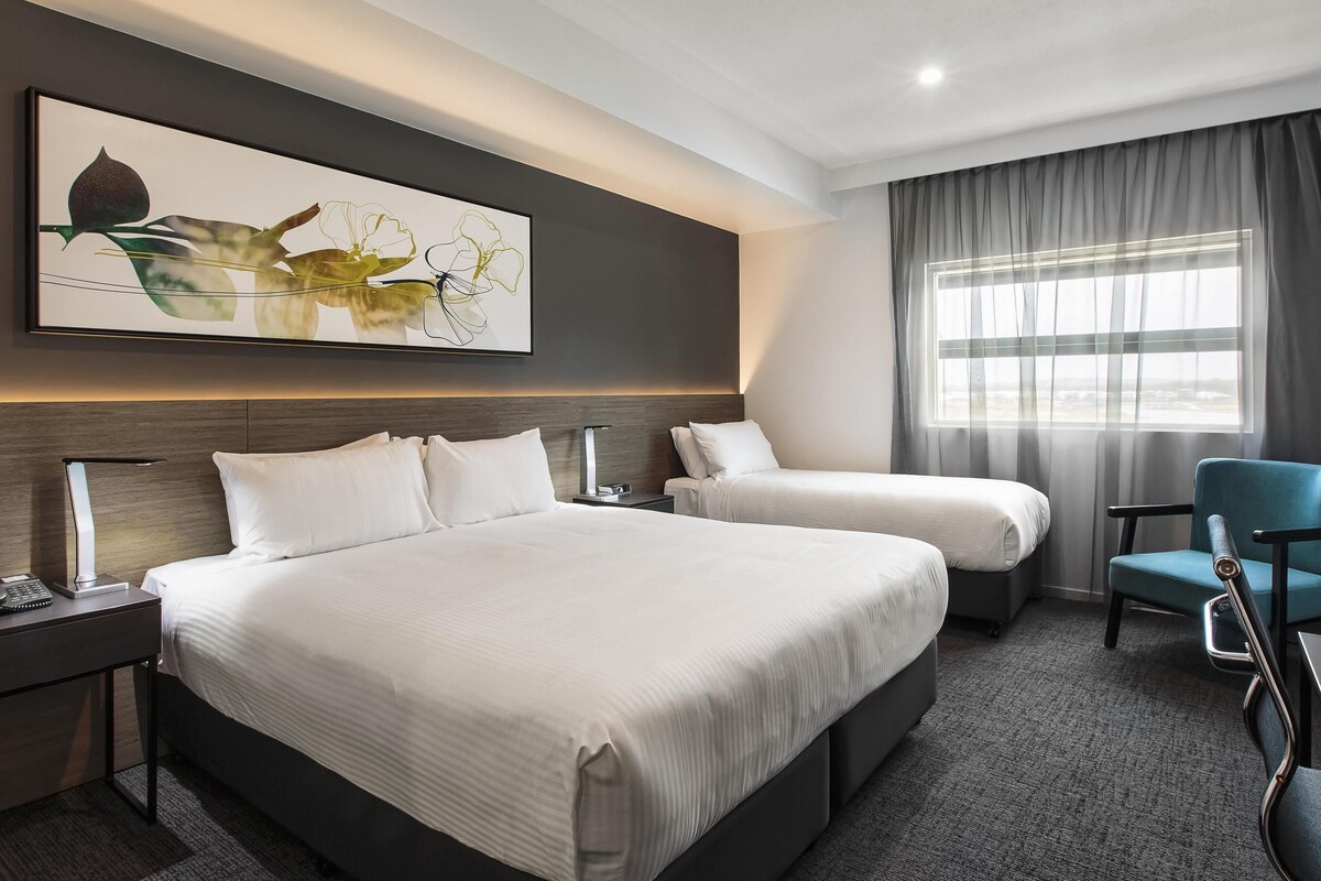 A hotel room with a large bed, a smaller bed, a desk, a chair, and a window with curtains.