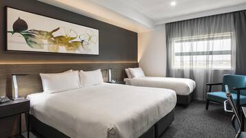 Ein Hotelzimmer mit einem großen Bett, einem Einzelbett, einem Schreibtisch, einem Sessel und einem Fenster mit Vorhängen.