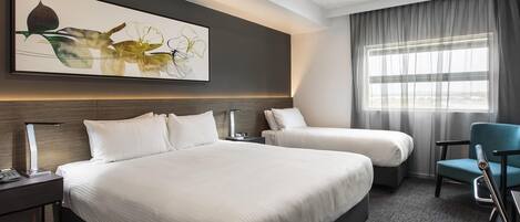Une chambre d’hôtel avec un grand lit, un lit plus petit, un bureau, une chaise et une fenêtre avec des rideaux.