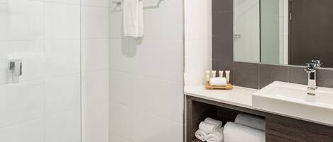 Une salle de bain moderne avec une douche à l’italienne en verre, un lavabo blanc doté d’un plan de toilette foncé et un grand miroir au-dessus du lavabo.