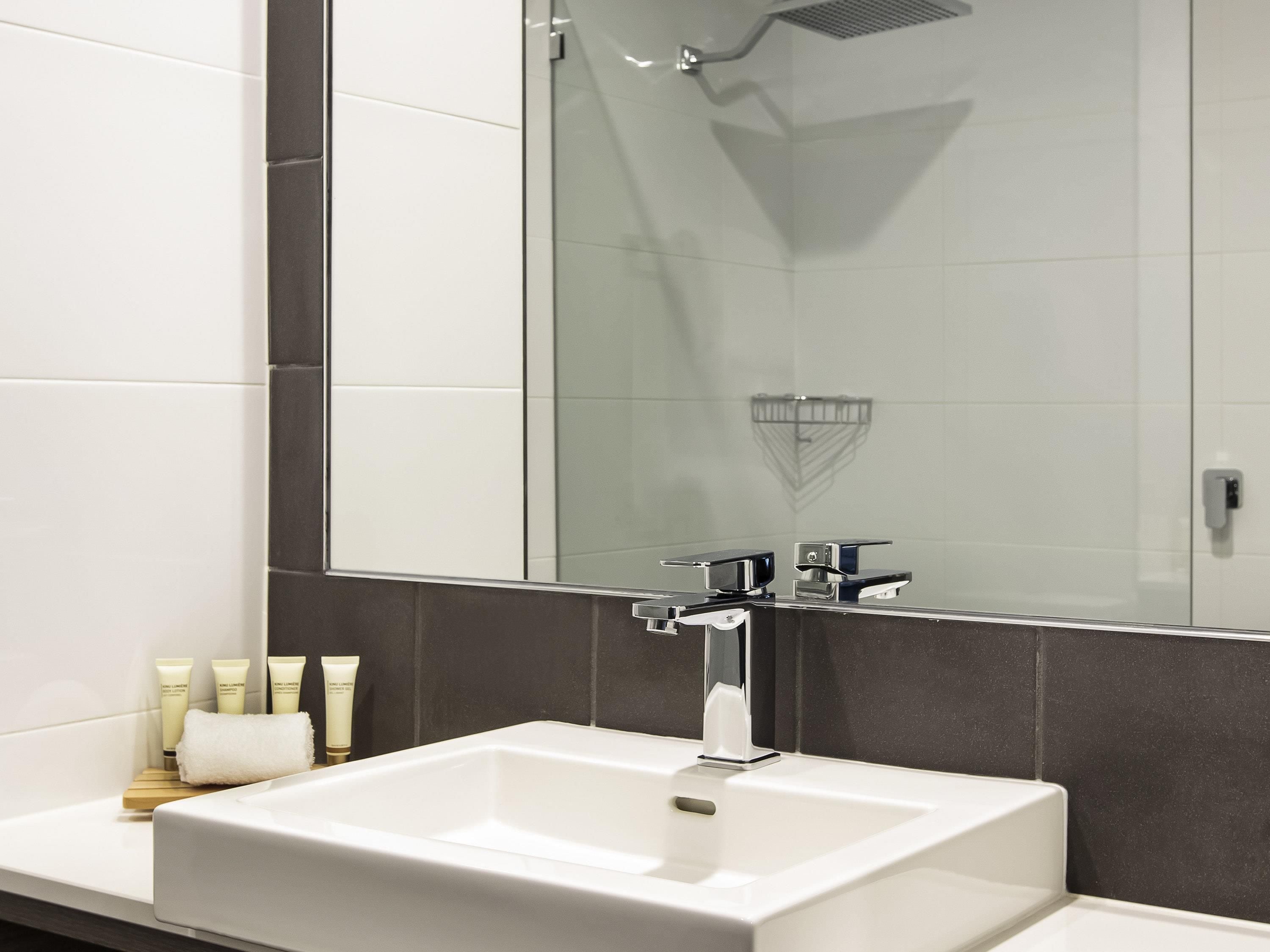 A modern bathroom with a large mirror, a white sink, and a shower.